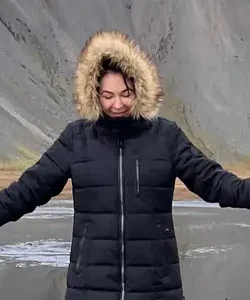 Woman in a fur-hooded winter jacket with arms open on a beach