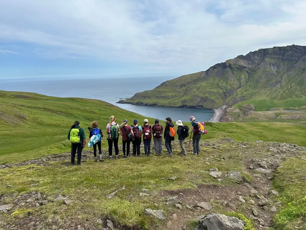 Line of hikers crossing a green hillside above the sea
