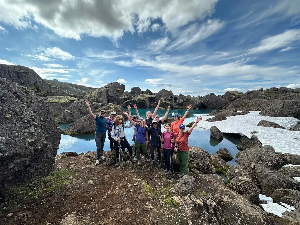 Group of hikers cheering by a turquoise lake among snowy rocks