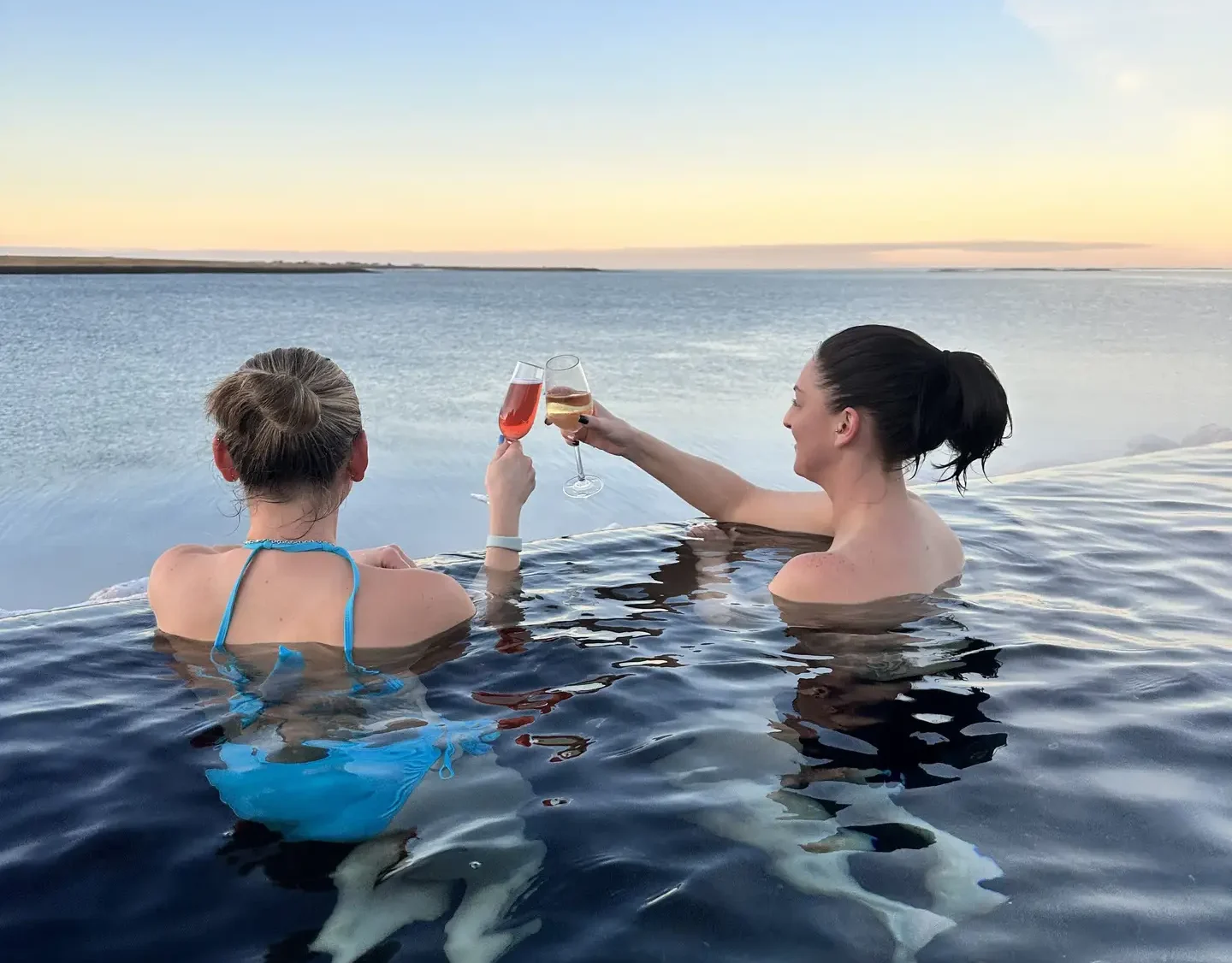 Two women with drinks in an infinity pool overlooking the sea