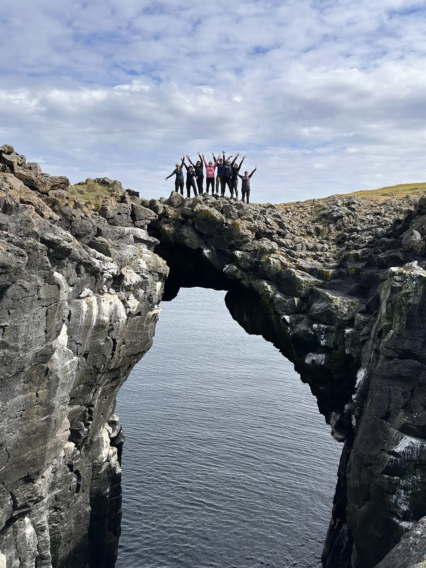 Group standing on top of a natural rock arch above the sea