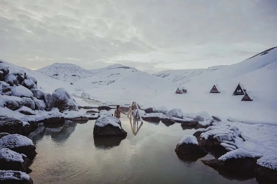 Rocky shoreline with ice and snowy hills reflected in still water