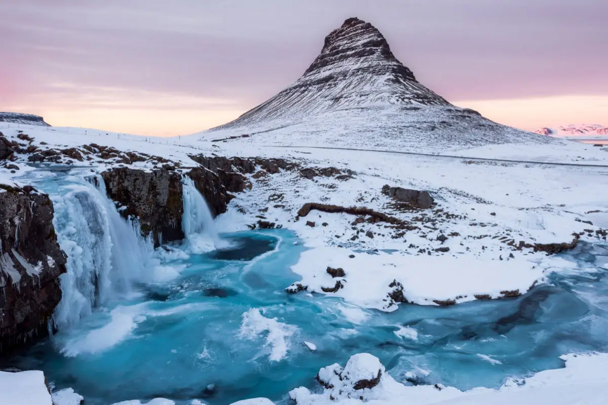 Snowy cone-shaped mountain above a waterfall in winter