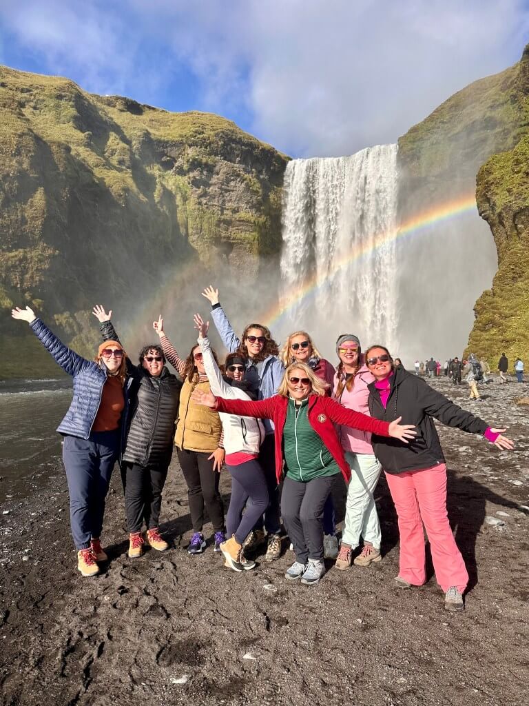 Group of women cheering in front of a waterfall with a rainbow