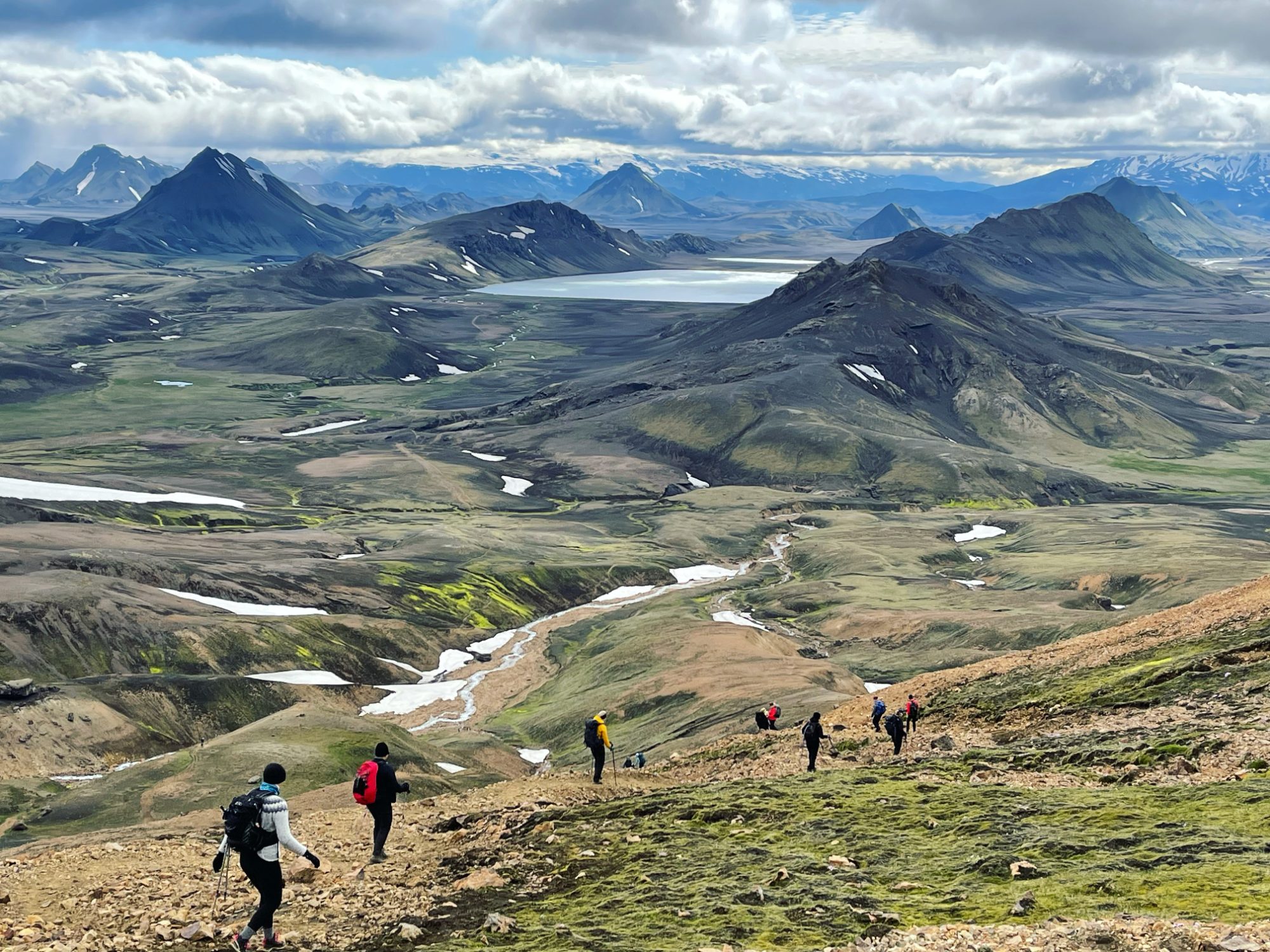 Hikers on a trail through green highlands with lakes and mountains