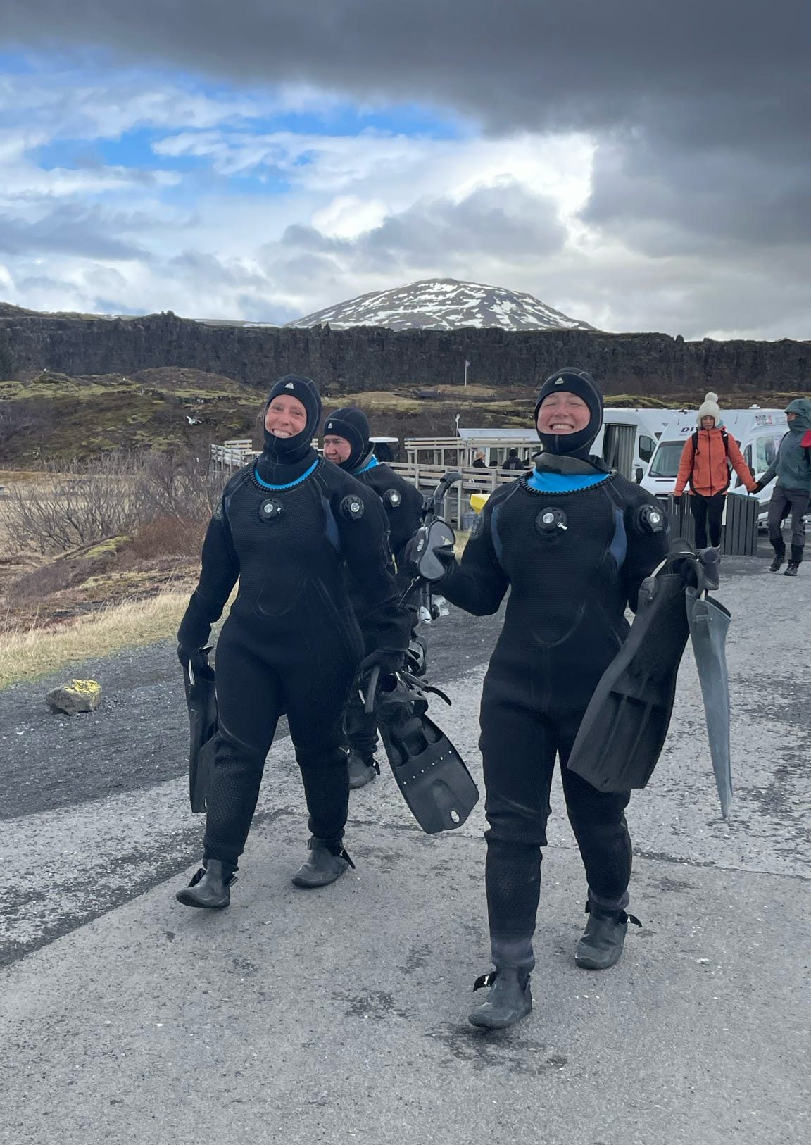 Two women in drysuits carrying snorkel fins