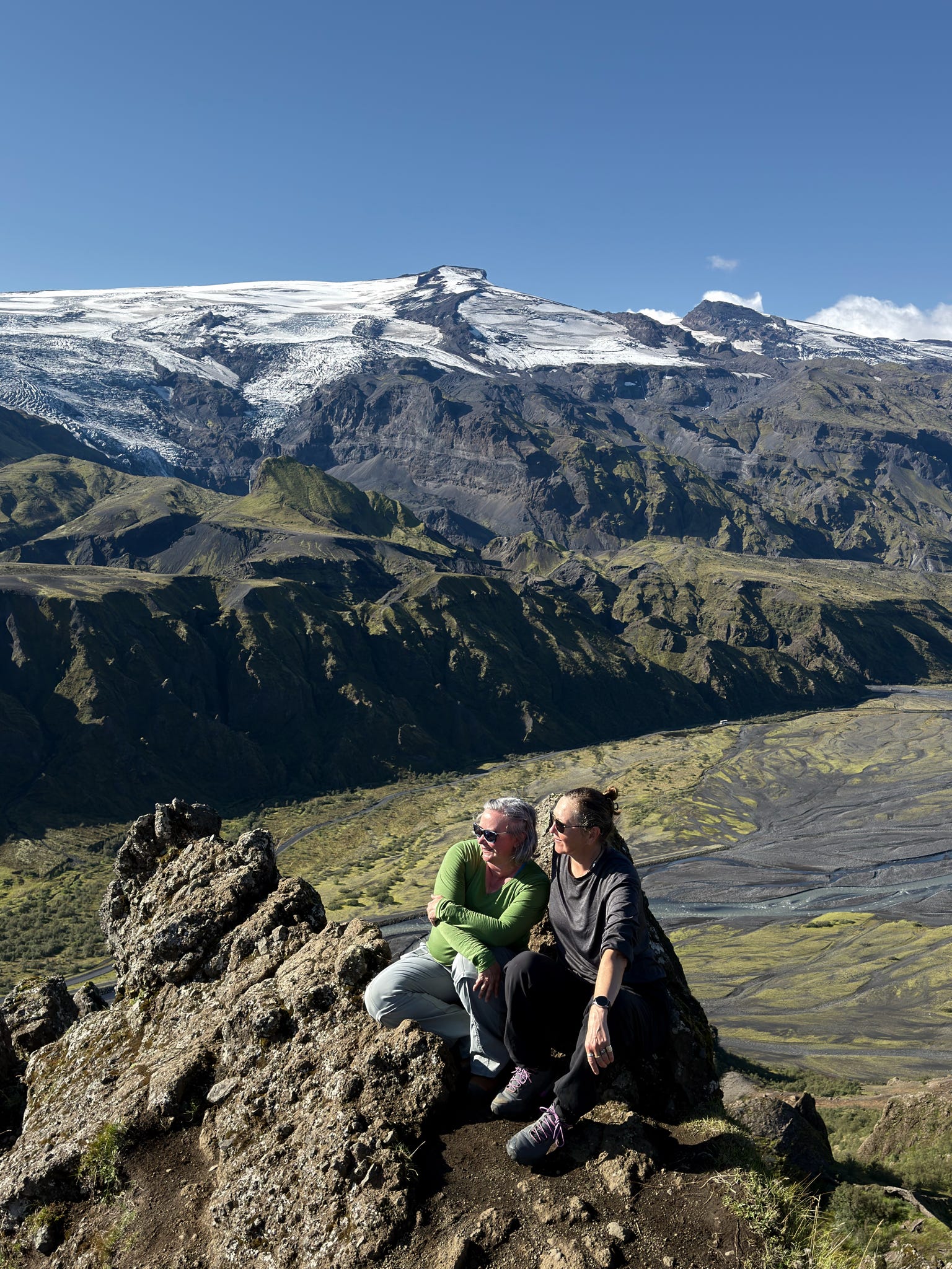 Two women sitting on a rock above a valley with a snowy glacier