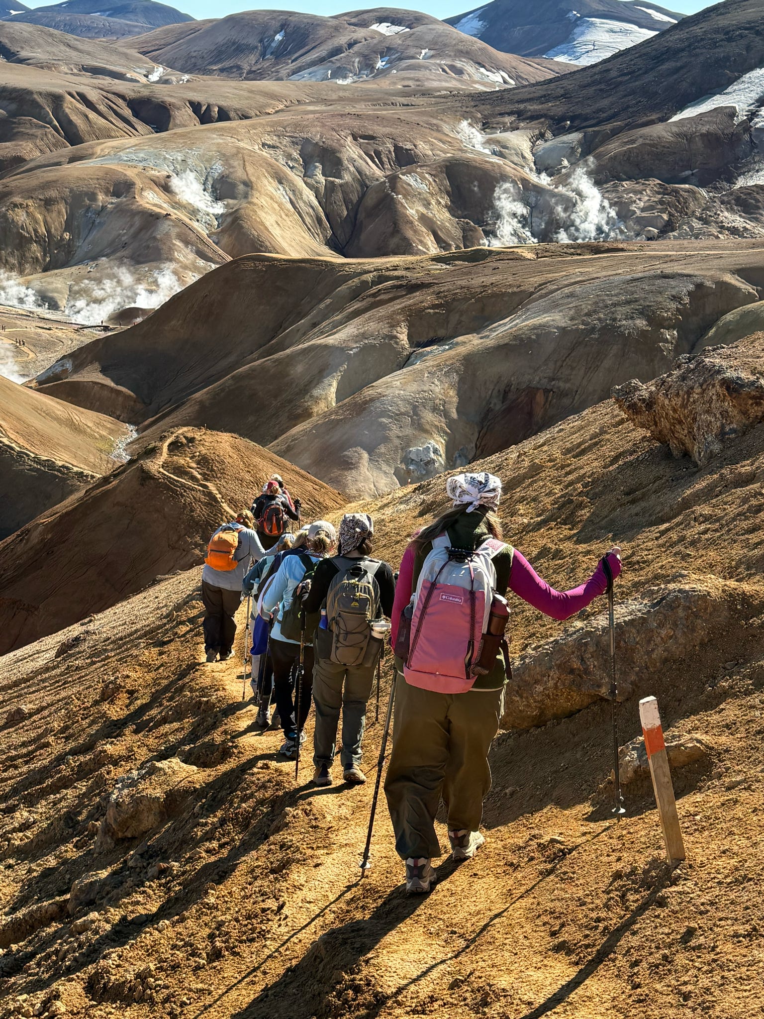Hikers on a trail through colorful geothermal hills