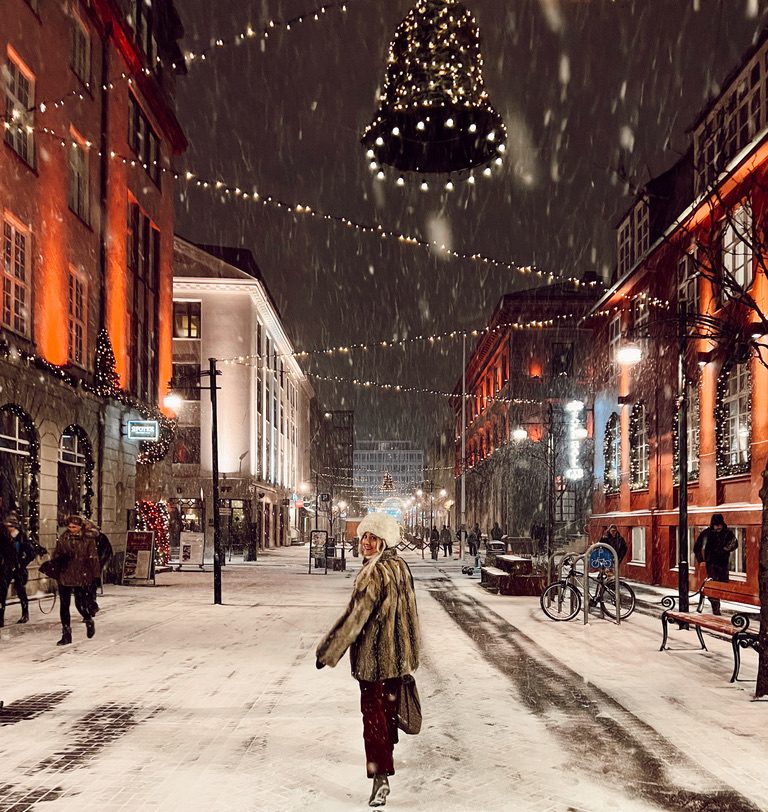 Woman walking down a snowy street with Christmas lights