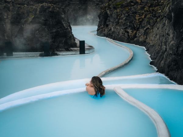 Woman bathing in a milky blue geothermal pool between lava rocks