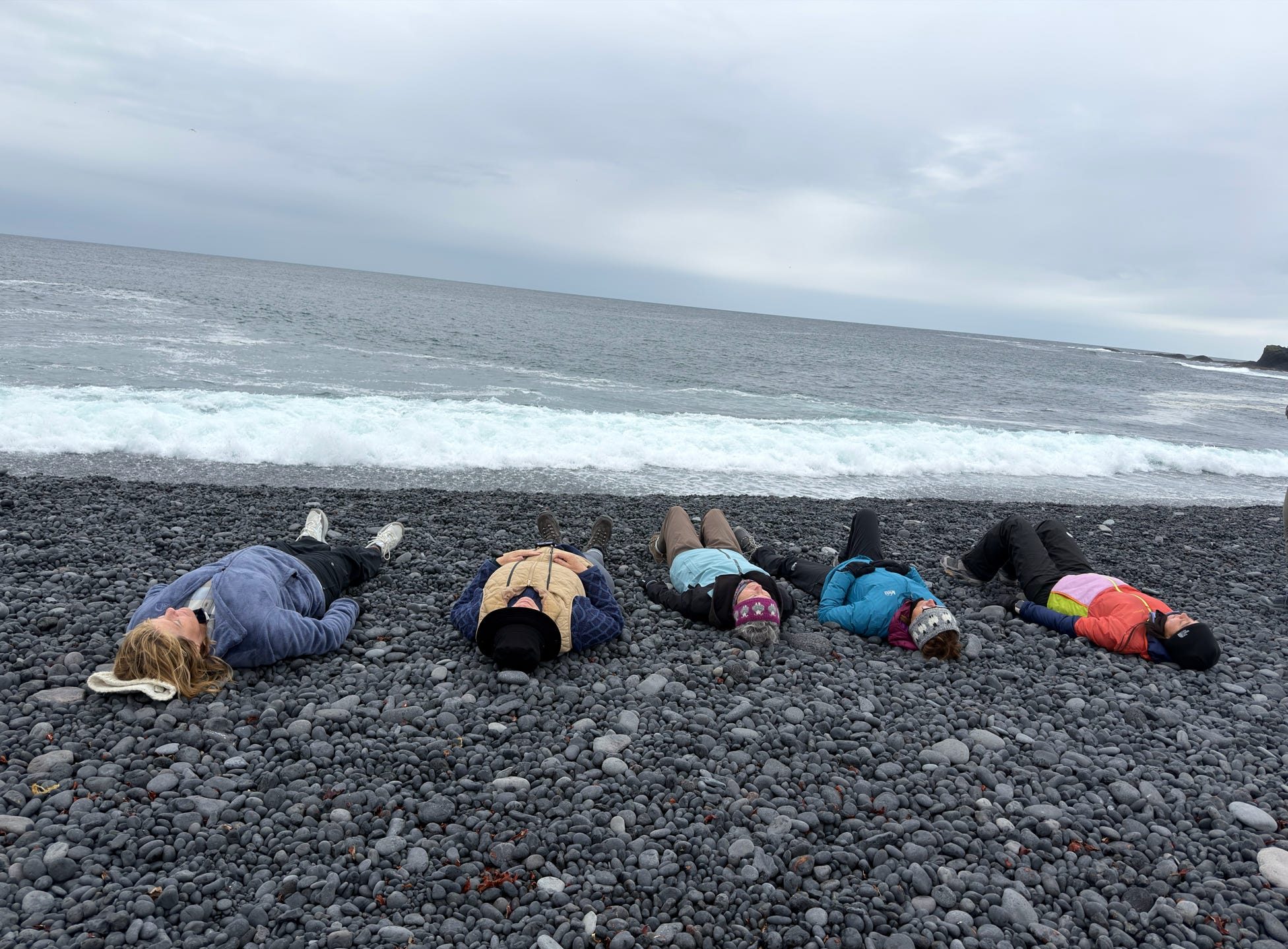 Group of women lying on a black pebble beach by the sea