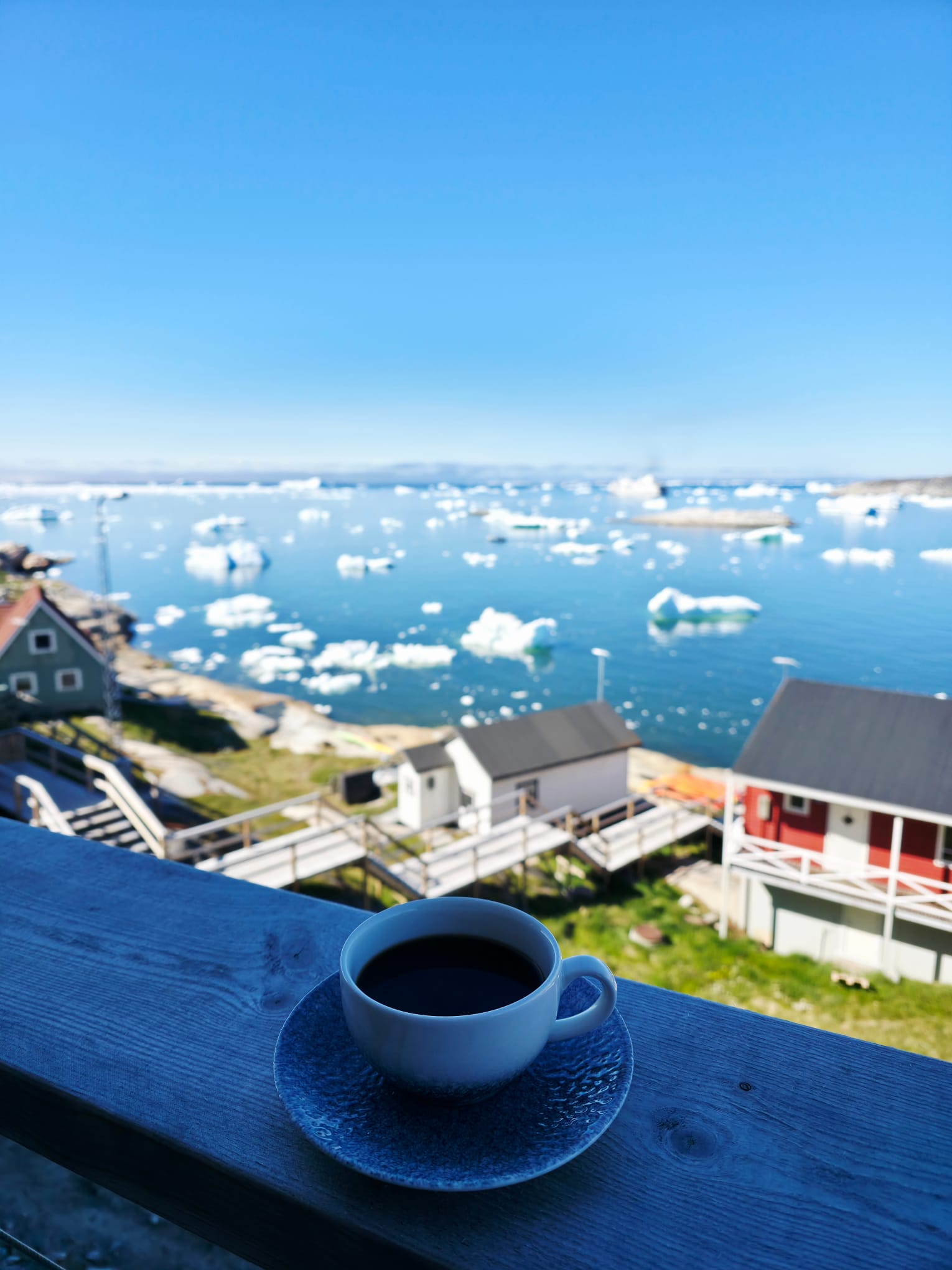 Cup of coffee on a terrace overlooking an icefjord and houses