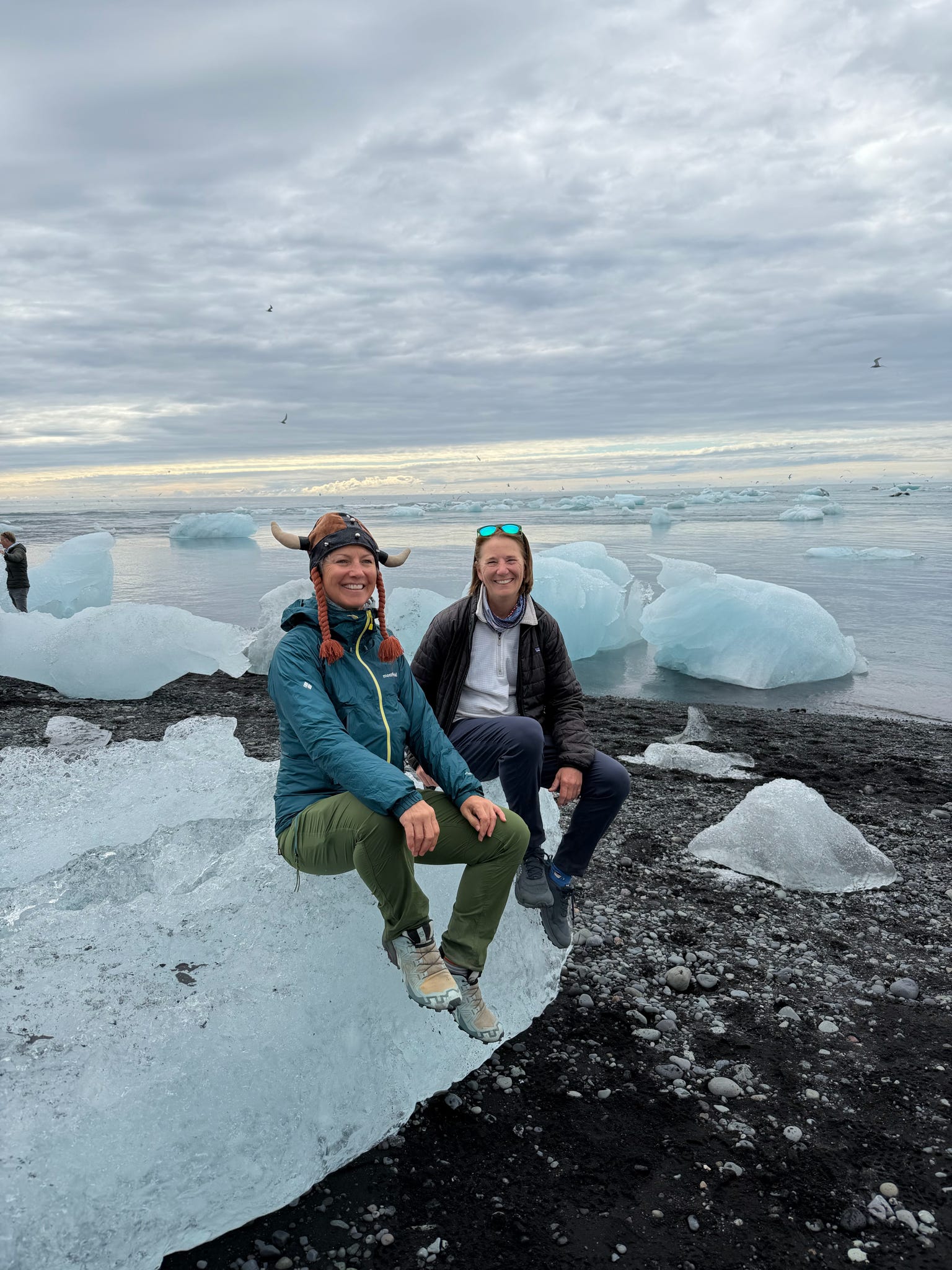 Two women sitting on an iceberg on a black sand beach
