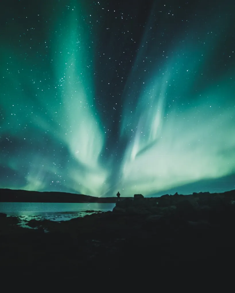 Green northern lights over dark hills