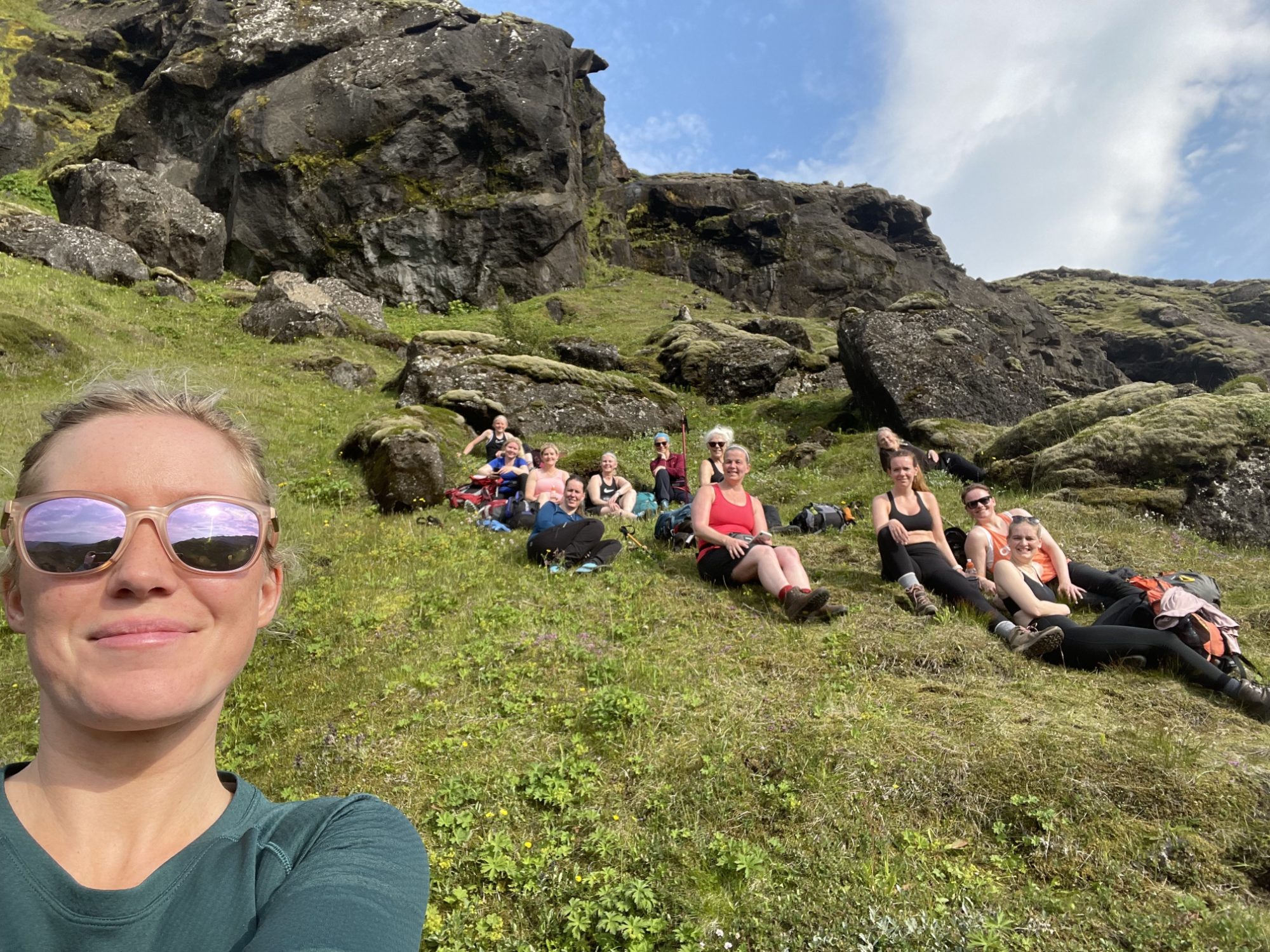 Woman taking a selfie with hikers resting on a grassy slope