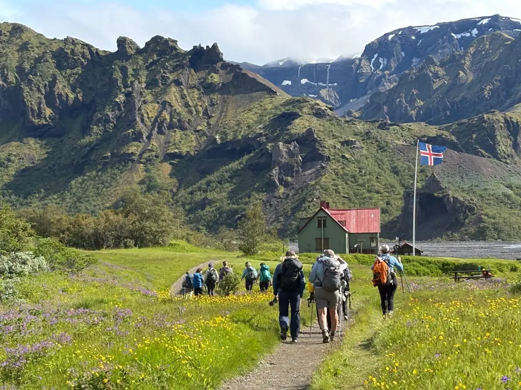 Hikers walking toward a red-roofed mountain hut in a green valley