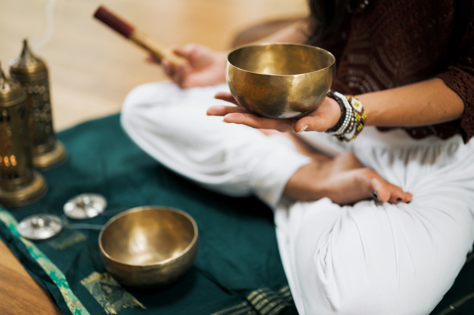 A person holding a brass singing bowl while sitting on a green cloth